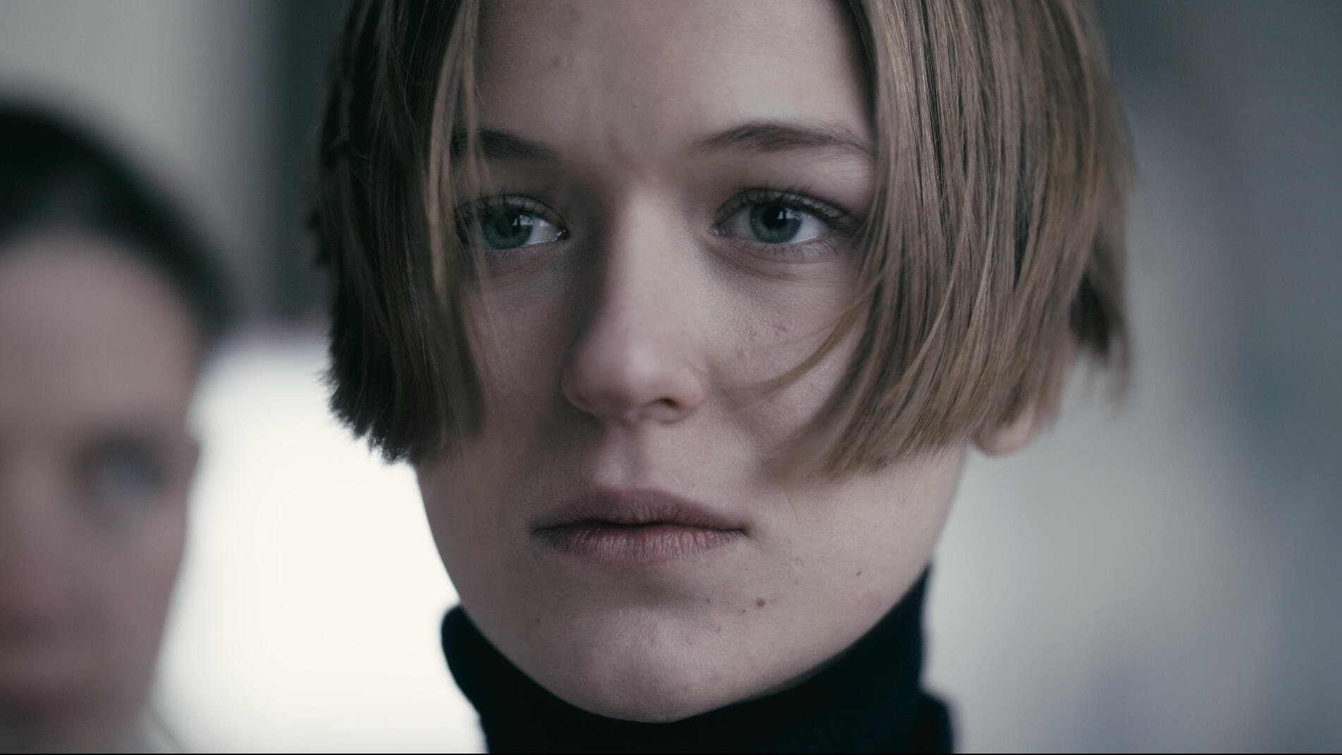 Nacházíme se v krajině vytvořené člověkem. Sledujeme hlouček pochodujícíh lidí strojově vykonávající stejné pohyby. Všichni jsou stejně oblečení a celkový jejich vzhled dává tušit, že zde není místo pro to, aby se někdo výrazně odlišoval. Skupina se zastav